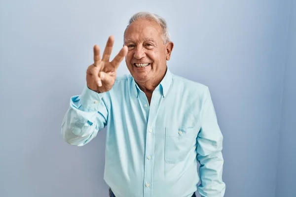 一个白发苍苍的老人站在蓝色的背景上 用第三指尖 面带微笑 自信而快乐 — 图库照片