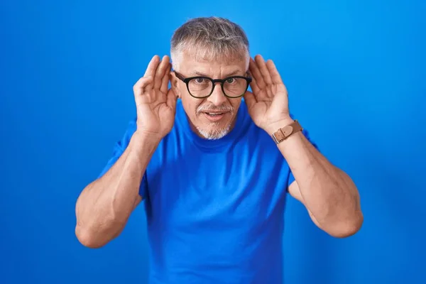 Homem Hispânico Com Cabelos Grisalhos Sobre Fundo Azul Tentando Ouvir — Fotografia de Stock