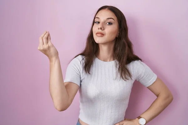 年轻的惊慌失措的姑娘站在粉红的背景上 手指手画脚地做着意大利式的手势 — 图库照片
