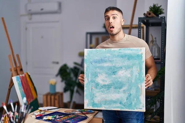 Young Hispanic Painter Man Holding Canvas Afraid Shocked Surprise Amazed — Stock Photo, Image