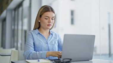 Genç sarışın iş kadını. Dizüstü bilgisayarda çalışırken kollarını kavuşturup ofiste el kol hareketi yapıyor.