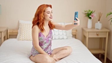 Genç kızıl saçlı kadın yatak odasında video görüşmesi yapıyor.