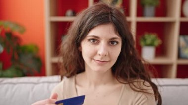 Evdeki kanepede oturan, elinde kredi kartı olan genç ve güzel bir İspanyol kadın.