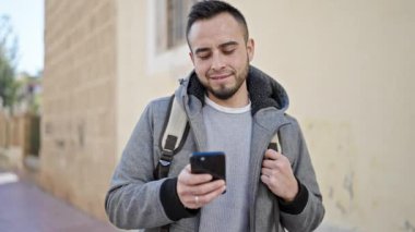 Hispanik adam sokakta gülümseyen akıllı telefon kullanıyor.