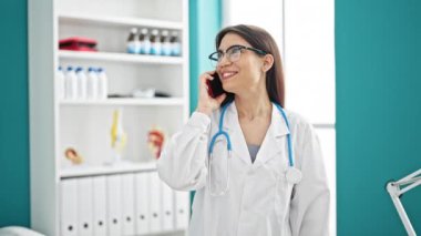 Genç, güzel İspanyol kadın doktor. Akıllı telefondan konuşuyor. Klinikte gülümsüyor.