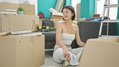 Genç ve güzel İspanyol kadın, yeni evinde kazanan yüz ifadesiyle yerde oturuyor.