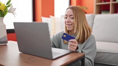 Genç sarışın kadın laptop ve kredi kartıyla alışveriş yapıyor.