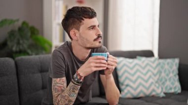 Genç İspanyol adam evdeki kanepede kahve içiyor.