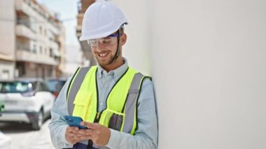 Kafkasyalı genç mimar inşaat alanında akıllı telefon kullanarak gülümsüyor.