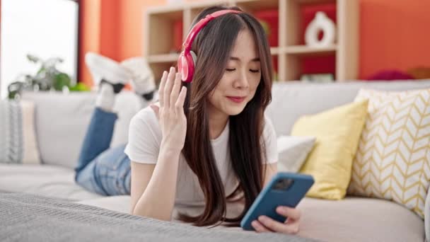 Νεαρή Κινέζα Γυναίκα Που Χρησιμοποιεί Smartphone Φορώντας Ακουστικά Ξαπλωμένη Στον — Αρχείο Βίντεο