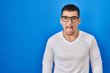 Gündelik beyaz gömlek giyen ve gözlüklü genç bir Arap komik bir ifadeyle dilini dışarı çıkartıyor. duygu kavramı. 