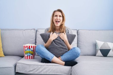 Güzel sarışın kadın TV seyrediyor. Kızgın ve kızgın bir şekilde bağırıyor. Öfkeyle bağırıyor.. 