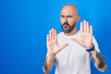 Mavi arka planda duran İspanyol dövmeli bir adam. Avuçlarını hareket ettiriyor. Korkmuş ve iğrenç bir ifadeyle reddediyor. Dur ve yasakla. 