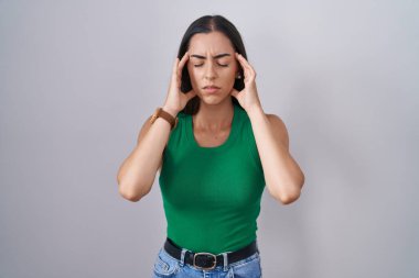 Tecrit edilmiş arka planda duran genç bir kadın, elleri başının üstünde, stres yüzünden baş ağrısı. migren ağrısı. 