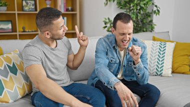 İki erkek kanepede oturup evde şarkı söylüyor.