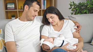 Üç kişilik bir aile evdeki kanepede oturup emziriyor.