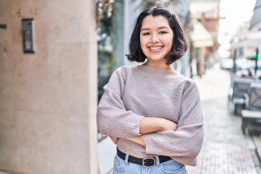 Young woman standing with arms crossed gesture looking to the camera at street