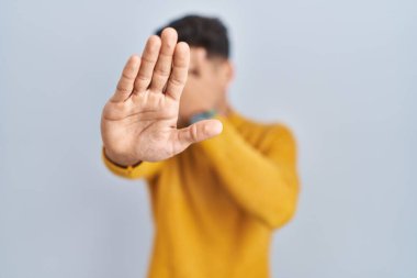 Young hispanic man standing over blue background covering eyes with hands and doing stop gesture with sad and fear expression. embarrassed and negative concept. 