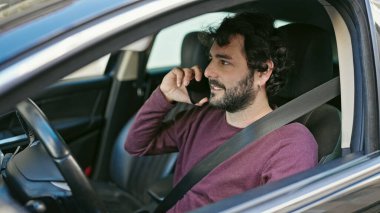 Genç İspanyol adam akıllı telefondan konuşuyor. Sokakta arabada oturuyor.