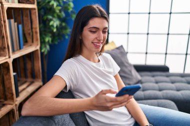 Evdeki kanepede oturan akıllı telefon kullanan genç, güzel İspanyol kadın.