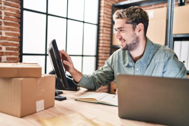 Young man ecommerce business worker writing on notebook touching screen computer at office