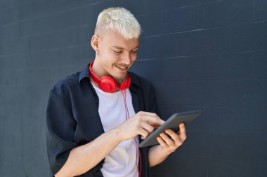 Young caucasian man using touchpad wearing headphones at street