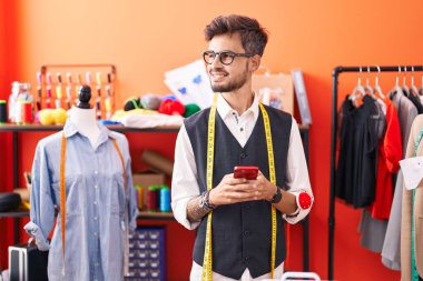 Genç İspanyol terzi atölyedeki akıllı telefonu kullanarak gülümsüyor.