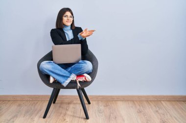 Sandalyeye oturmuş bilgisayar laptopu kullanan genç bir kadın avuç içi açık bir şekilde fotokopi alanını gösteriyor, gülümseyerek mutlu bir şekilde gülümsüyor. 