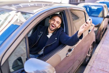 Young hispanic man smiling confident holding key of new car at street