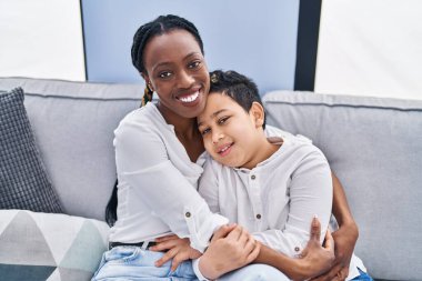 African american mother and son hugging each other sitting on sofa at home