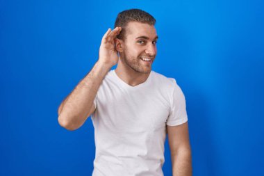 Mavi arka planda dikilmiş, ağzı kulaklarında dolaşan genç bir beyaz adam dedikoduları ve dedikoduları dinliyor. Sağırlık kavramı. 