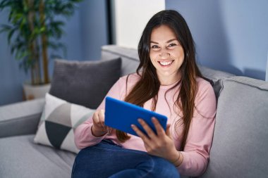 Evdeki koltukta oturan dokunmatik ped kullanan genç bir kadın.