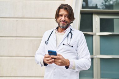 Hastanedeki akıllı telefonu kullanarak gülümseyen orta yaşlı bir doktor.