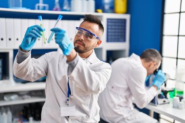 Two men scientists holding test tubes using microscope at laboratory