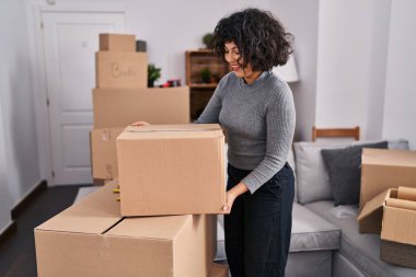 Young beautiful hispanic woman smiling confident holding package at new home