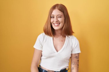 Sarı arka planda duran genç kızıl saçlı kadın kameraya seksi bir ifadeyle bakıyor, neşeli ve mutlu bir yüzle.. 
