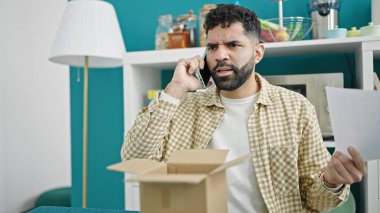Genç İspanyol adam yemek odasında karton kutuları açarken akıllı telefondan tartışıyor.