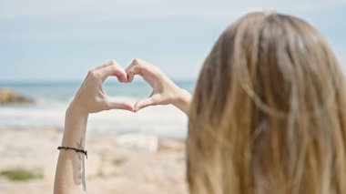 Genç sarışın turist plajda kalp hareketi yapıyor.