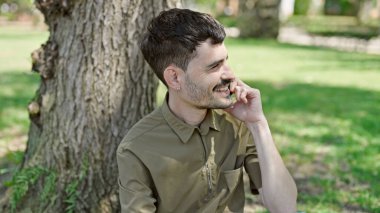 Genç İspanyol adam akıllı telefondan konuşuyor. Parkta oturuyor.