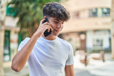 Latin kökenli genç, gülümsüyor ve caddede akıllı telefondan konuşuyor.