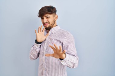 Mavi arka planda duran sakallı bir Arap, tiksindirici bir ifade, tiksindirici bir yüz ifadesi, tiksindirici bir ifade.. 