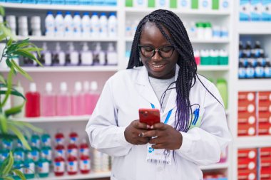 Eczanede çalışan akıllı telefonu kullanan Afrikalı Amerikalı kadın eczacı.