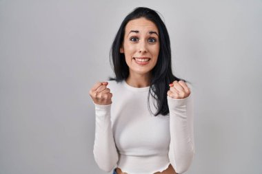 Tecrit edilmiş arka planda dikilen İspanyol kadın şaşkınlığı ve şaşkınlığı kollarını kaldırarak ve gözlerini açarak kutluyor. Kazanan konsept. 
