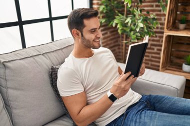 Evdeki kanepede oturmuş kitap okuyan genç bir İspanyol.