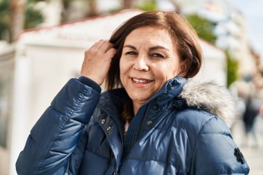 Orta yaşlı bir kadın sokakta kendine güvenerek gülümsüyor.