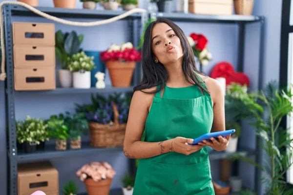 Brunette woman working at florist shop holding tablet looking at the camera blowing a kiss being lovely and sexy. love expression.