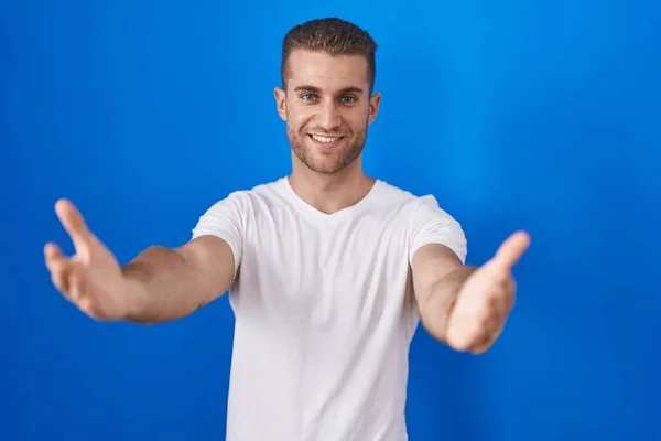 青い背景の上に立つ若い白人男性笑顔陽気に手を提供援助と受け入れを与える — ストック写真