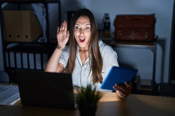 stock image Young brunette woman working at the office at night waiving saying hello happy and smiling, friendly welcome gesture 