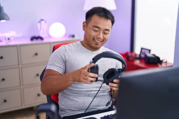Young Chinese Man Streamer Smiling Confident Holding Headphones Gaming Room - Stock-foto