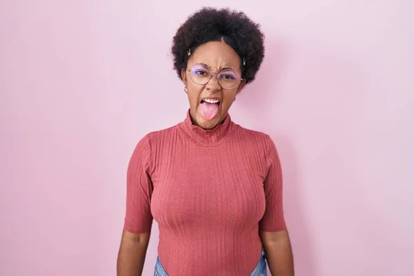 美丽的非洲女人 卷曲的头发站在粉红的背景上 带着滑稽的表情伸出舌头 情感概念 — 图库照片